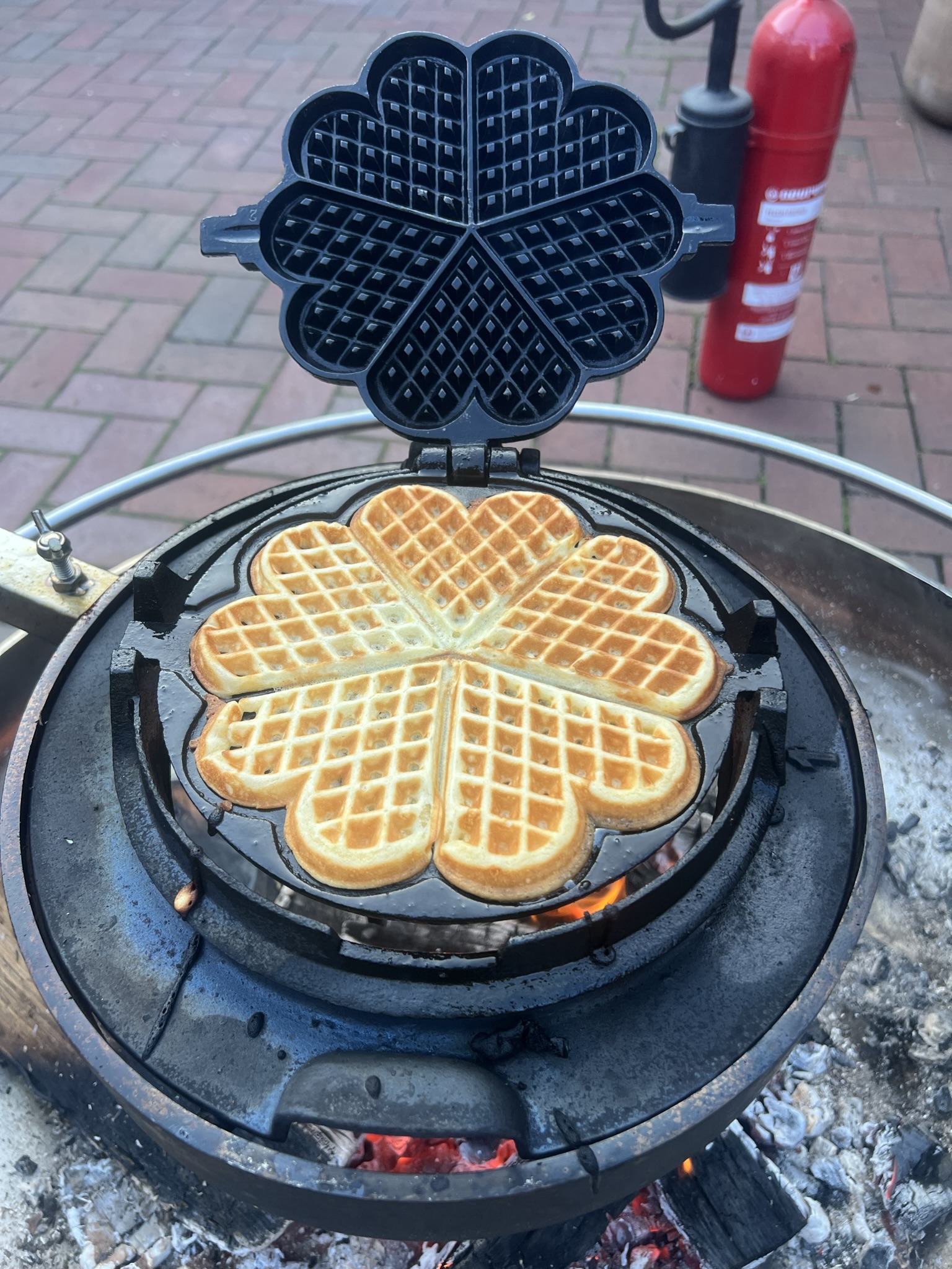 Goldbraune Herzwaffel im historischen gusseisernen Waffeleisen über offenem Feuer